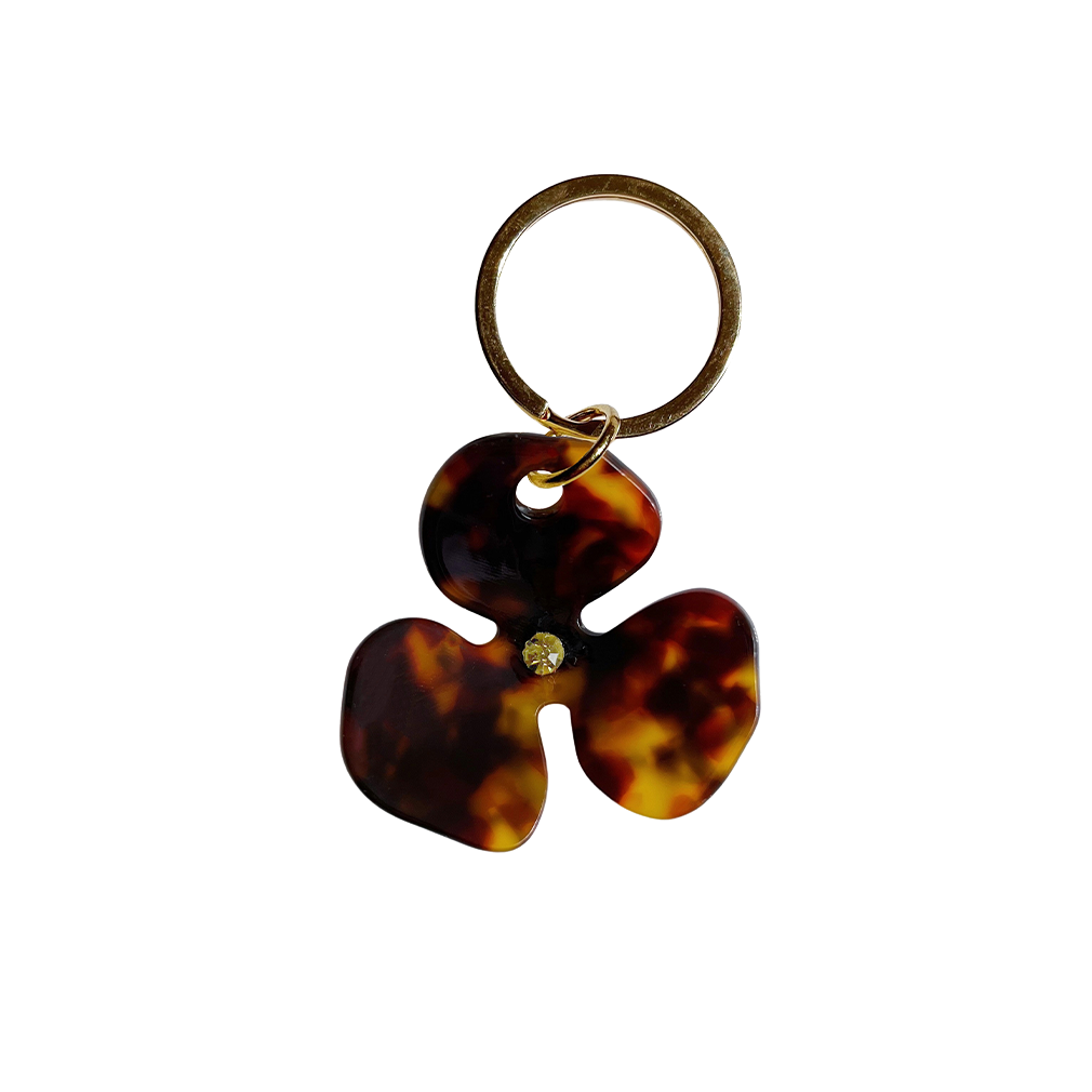 Meet FLOR!  A brown tortoiseshell flower with a green jewel in the centre and Tort logo embossed on the back. Complete with brass-gold keyring hardware so you're able to attach to keys.  Each keyring comes in a branded Tort pouch (colours change seasonally).  Size: 4.5cm  Colour: brown tortoiseshell with green jewel  Material: eco-resin 