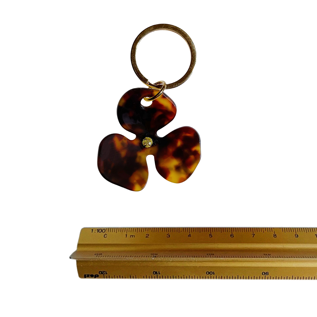 Meet FLOR!  A brown tortoiseshell flower with a green jewel in the centre and Tort logo embossed on the back. Complete with brass-gold keyring hardware so you're able to attach to keys.  Each keyring comes in a branded Tort pouch (colours change seasonally).  Size: 4.5cm  Colour: brown tortoiseshell with green jewel  Material: eco-resin 